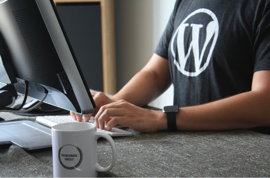 man wearing a black woocommerce t-shirt in front of a computer