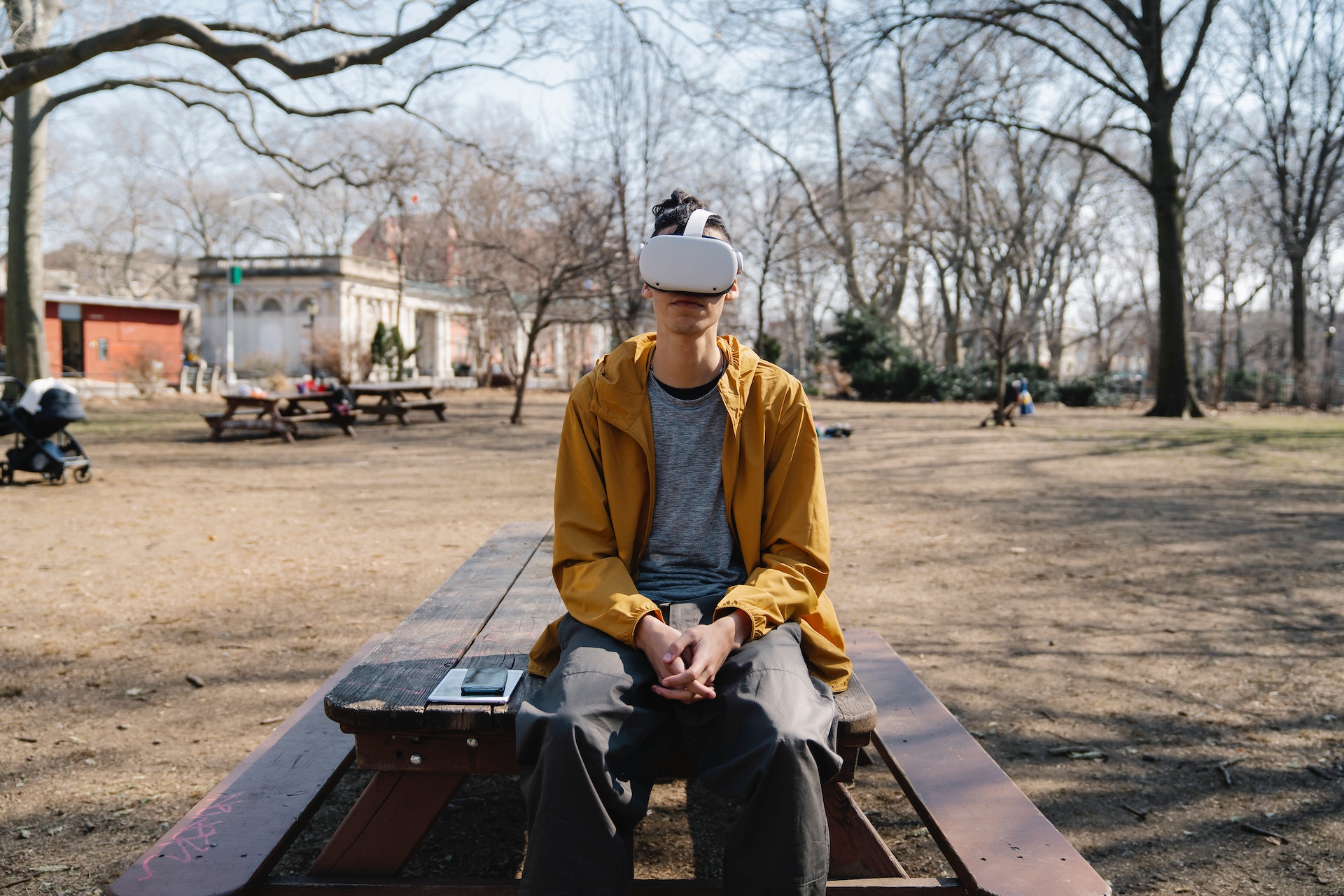 Young man sitting on bench in park with VR headset